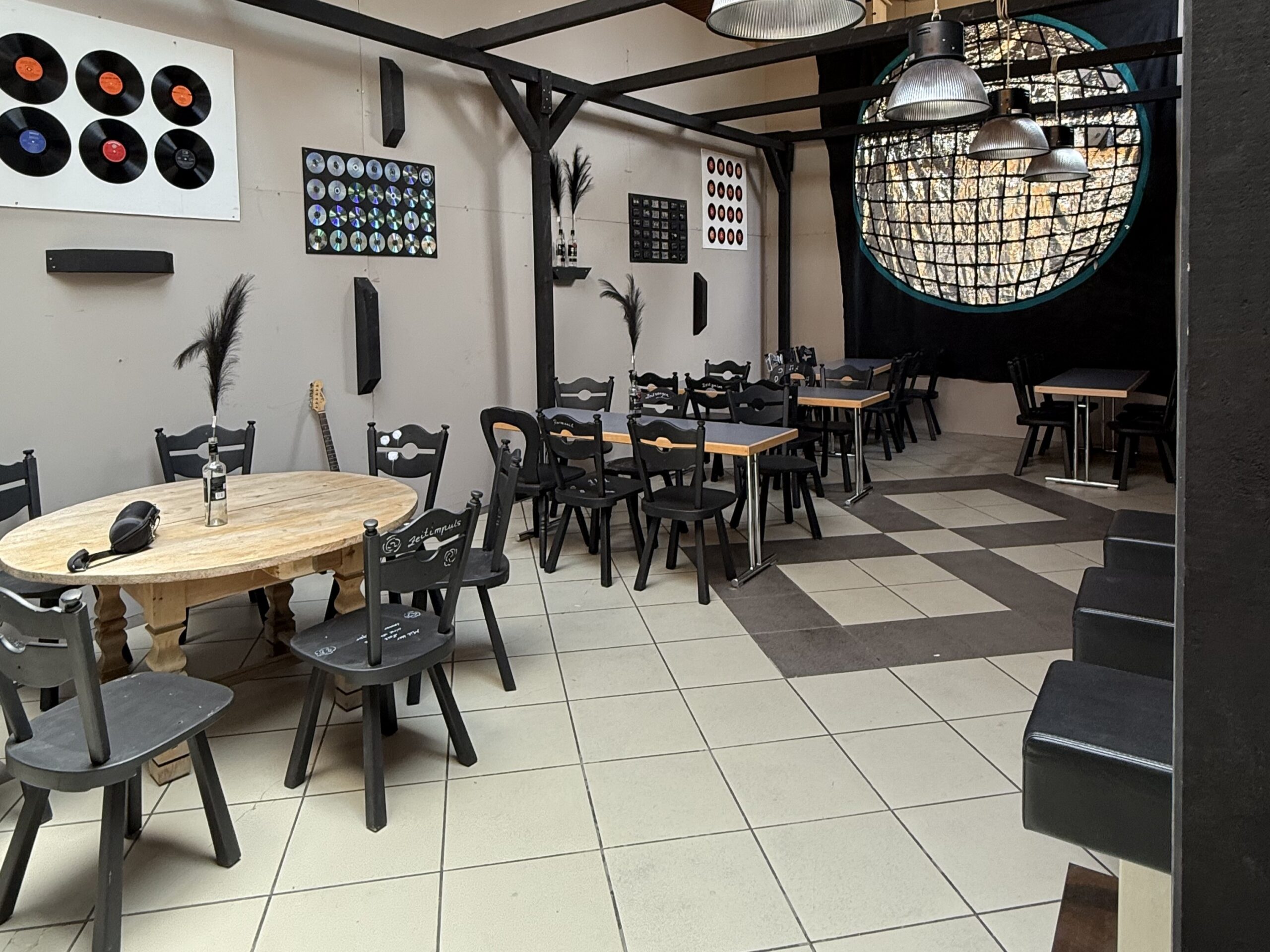 Ausstellung ZEITGeschichteN Umgestaltetes Foyer im Haus des Gastes mit Tischen, schwarzen Stühlen, einer Disckugel und Schallplatten an der Wand